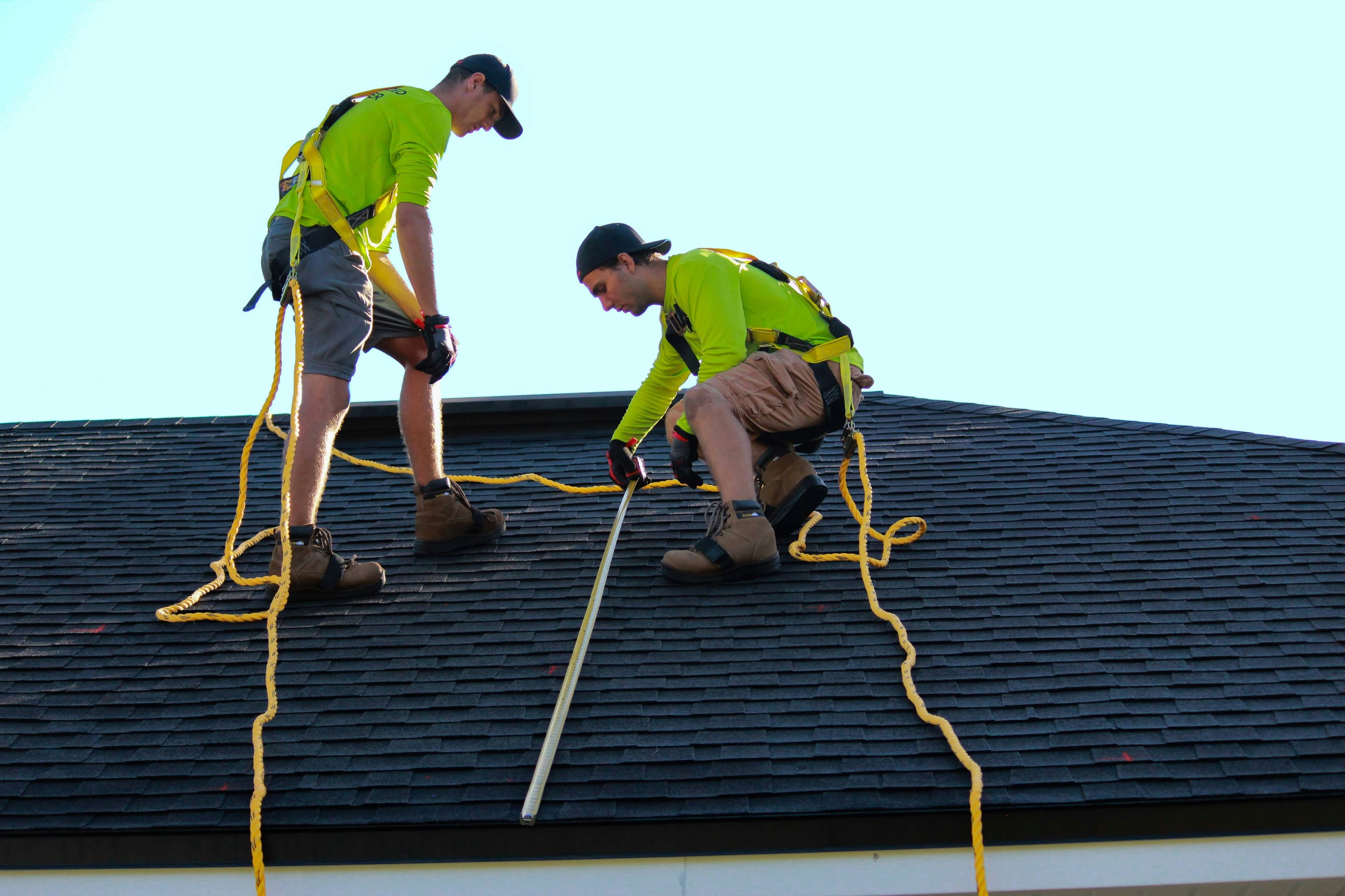 Roofing professionals inspecting and measuring a residential roof
